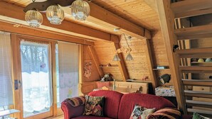A cozy cabin interior with a red sofa, a wooden dining table, and a large window with blinds. - Holiday Home 'Haus Paradiesecke' with Private Terrace, Garden and Wi-Fi (Waldbrunn)