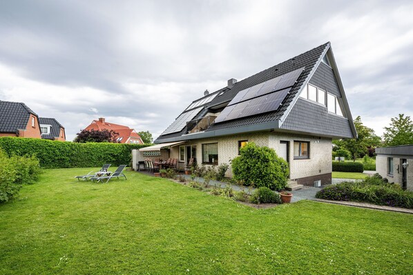A house with a sloped roof, solar panels, a well-maintained lawn, and a patio area.