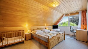 Una camera da letto con soffitto in legno, un letto, una scrivania, una sedia e una finestra con tende.