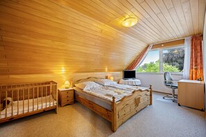 A bedroom with a wooden ceiling, a bed, a desk, a chair, and a window with curtains.