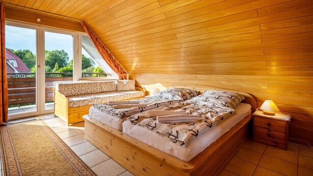 Una camera da letto in legno con un letto, un comodino, una panca e vista sull'esterno.