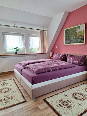 Una camera da letto con un letto, due finestre, un termosifone, un quadro e una pianta in vaso.