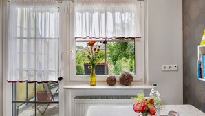 Et værelse med et vindue, en radiator, et bord med en vase blomster og en vandflaske.
