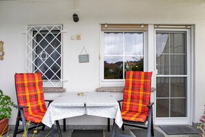 Un patio con dos sillas y una mesa, una ventana con vistas y una puerta.