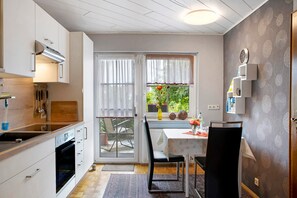 A modern kitchen with a dining area, a view through the window, and a clock on the wall. - The DTV Classified 3-Star Apartment Becker Zentrum with Private Terrace, Shared Garden (Lauterbach (Hessen))