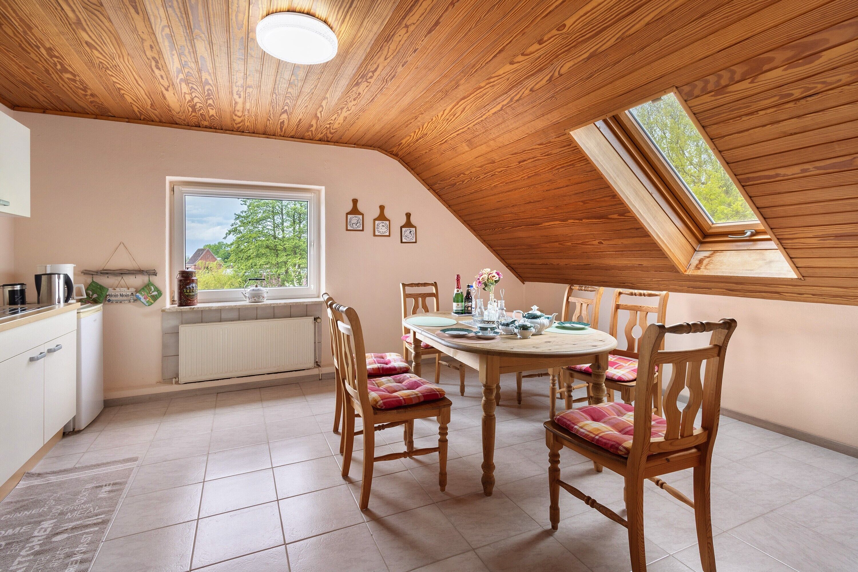 A dining area with a wooden ceiling, a round table, and chairs with plaid cushions.