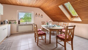 A dining area with a wooden ceiling, a round table, and chairs with plaid cushions.