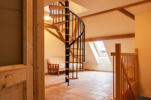 Una escalera de caracol con peldaños de madera y barandillas metálicas, que conduce a un dormitorio en entrepiso con techo inclinado y tragaluz.