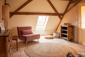 Un dormitorio tipo loft acogedor, con techo inclinado, cómoda de madera, sillón rosa mullido, alfombra tejida y aparador de madera rústica.