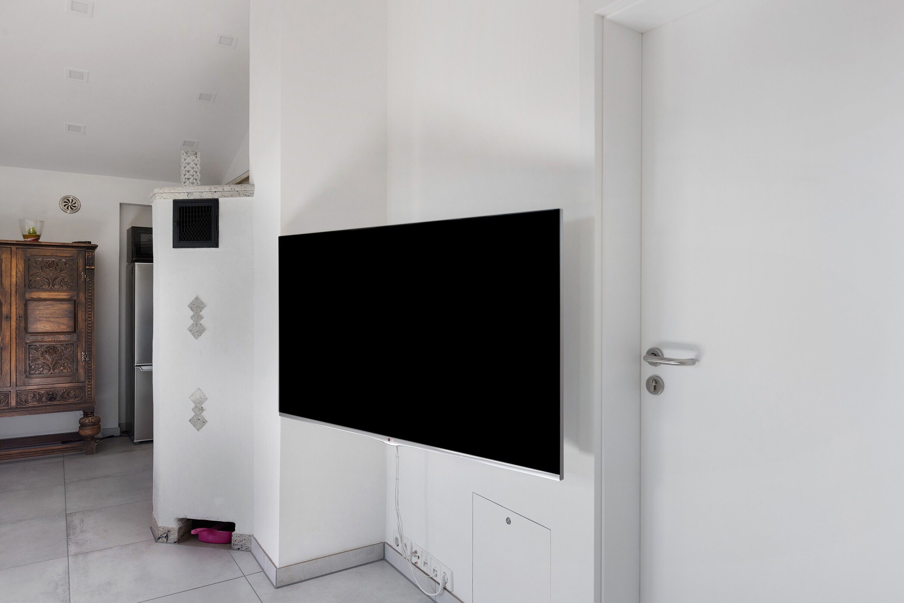 A room with a large flat-screen TV mounted on the wall, a wooden cabinet, and a door with a handle.