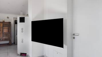 A room with a large flat-screen TV mounted on the wall, a wooden cabinet, and a door with a handle.