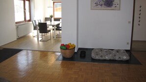 Een kamer met een eethoek, een aan de muur hangend schilderij, een dierenbedje en een mand met speelgoed.