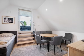 Une pièce de taille modeste comprenant un lit, une table à manger avec des chaises, un escalier et une fenêtre.
