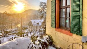 A building with a window and green shutters, surrounded by snow-covered ground and trees. - Apartment 'Wohnen Auf Dem Weingut - Klein Und Fein' with Shared Terrace, Shared Garden and Wi-Fi (Maring-Noviand)