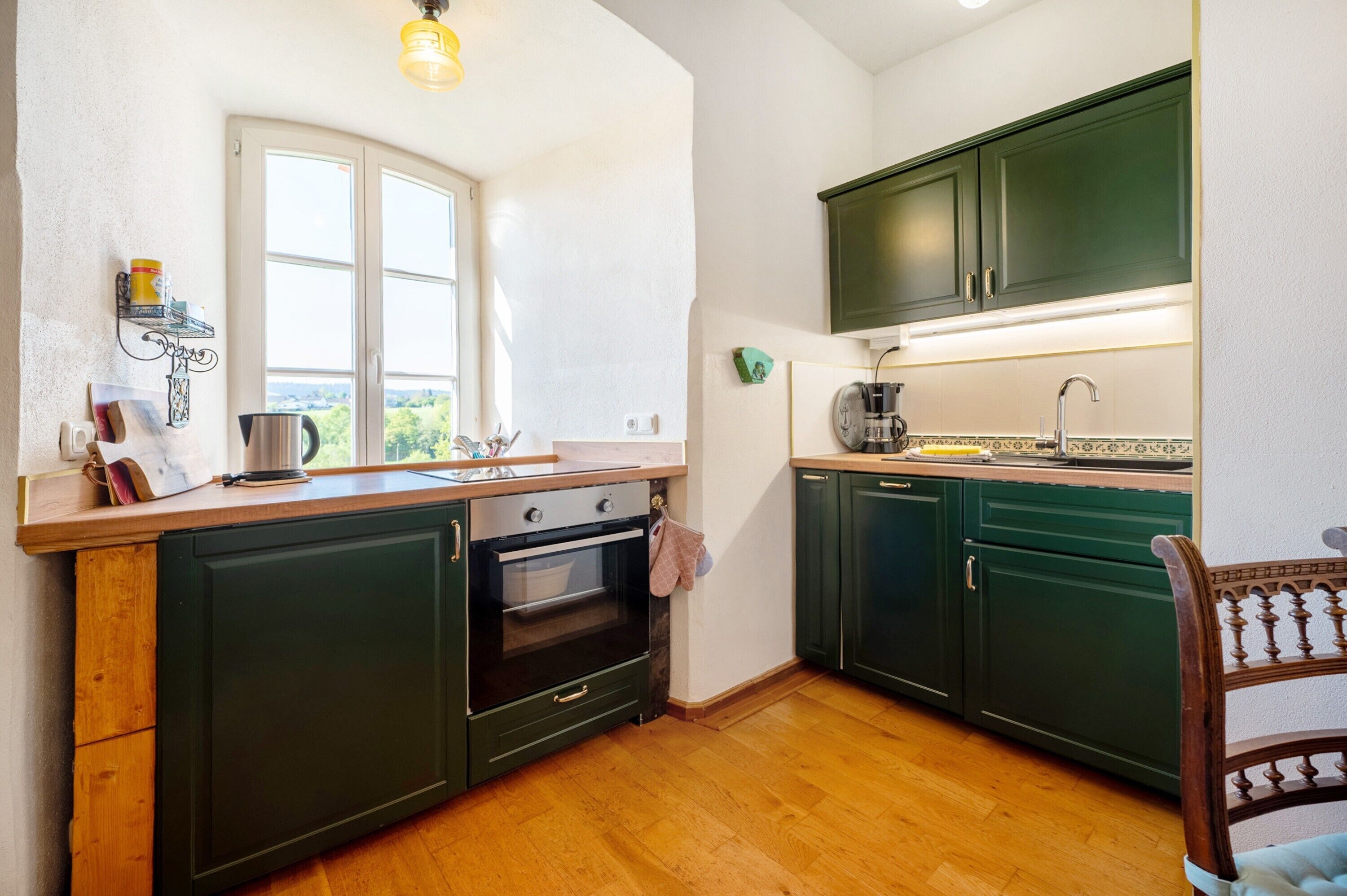 A kitchen with dark green cabinets, a wooden countertop, a window, and a view of greenery outside.