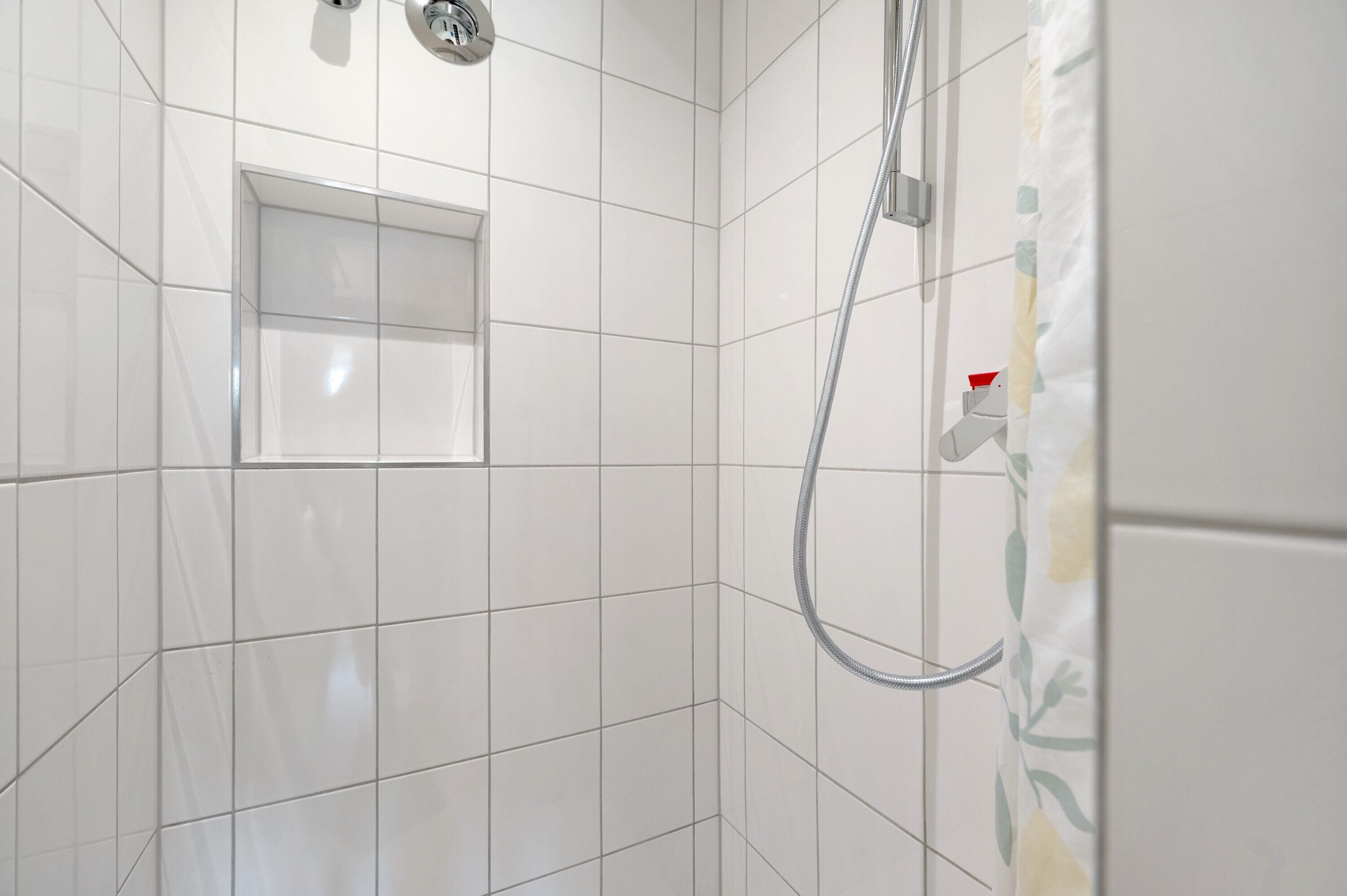 A shower area with white tiled walls, a showerhead, and a towel rack.