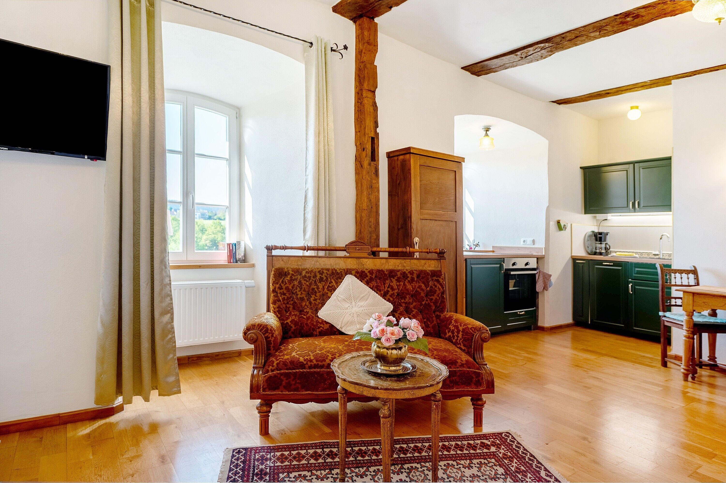 Una sala de estar con un sofá, una mesa de centro con un florero, un aparador de madera y una cocina al fondo.