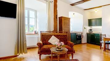 Una sala de estar con un sofá, una mesa de centro con un florero, un aparador de madera y una cocina al fondo.