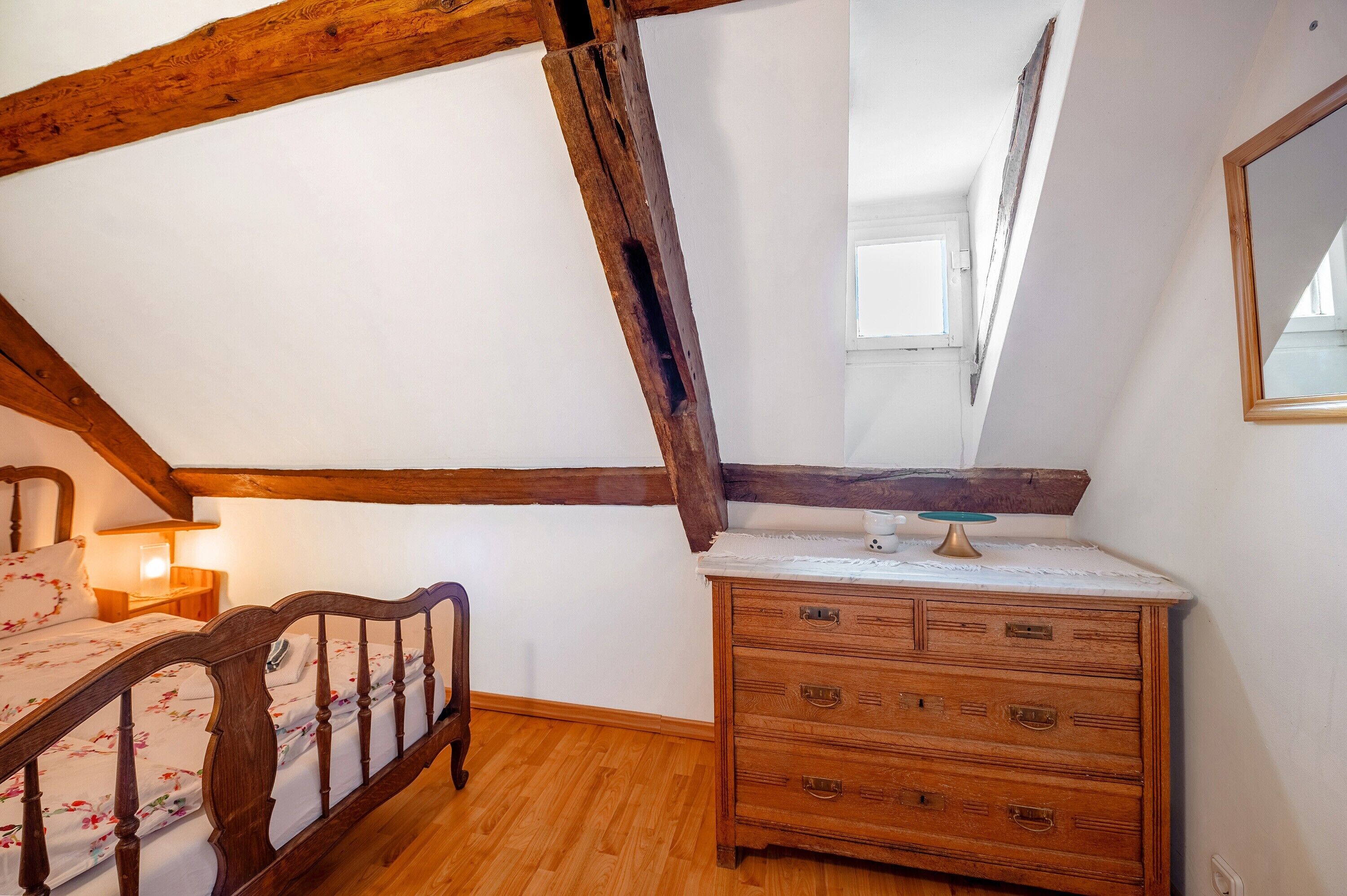 Un dormitorio con techo de madera, una cama con ropa de cama floral, un aparador y un espejo.