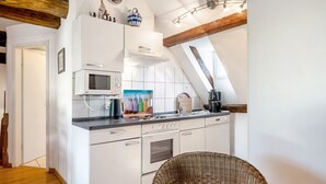 Een keuken met witte kastjes, een magnetron, een fornuis en een rieten stoel.