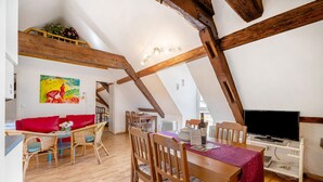 Een loft-stijl kamer met een houten plafond, een rode bank, rieten stoelen, een eettafel en een televisie.