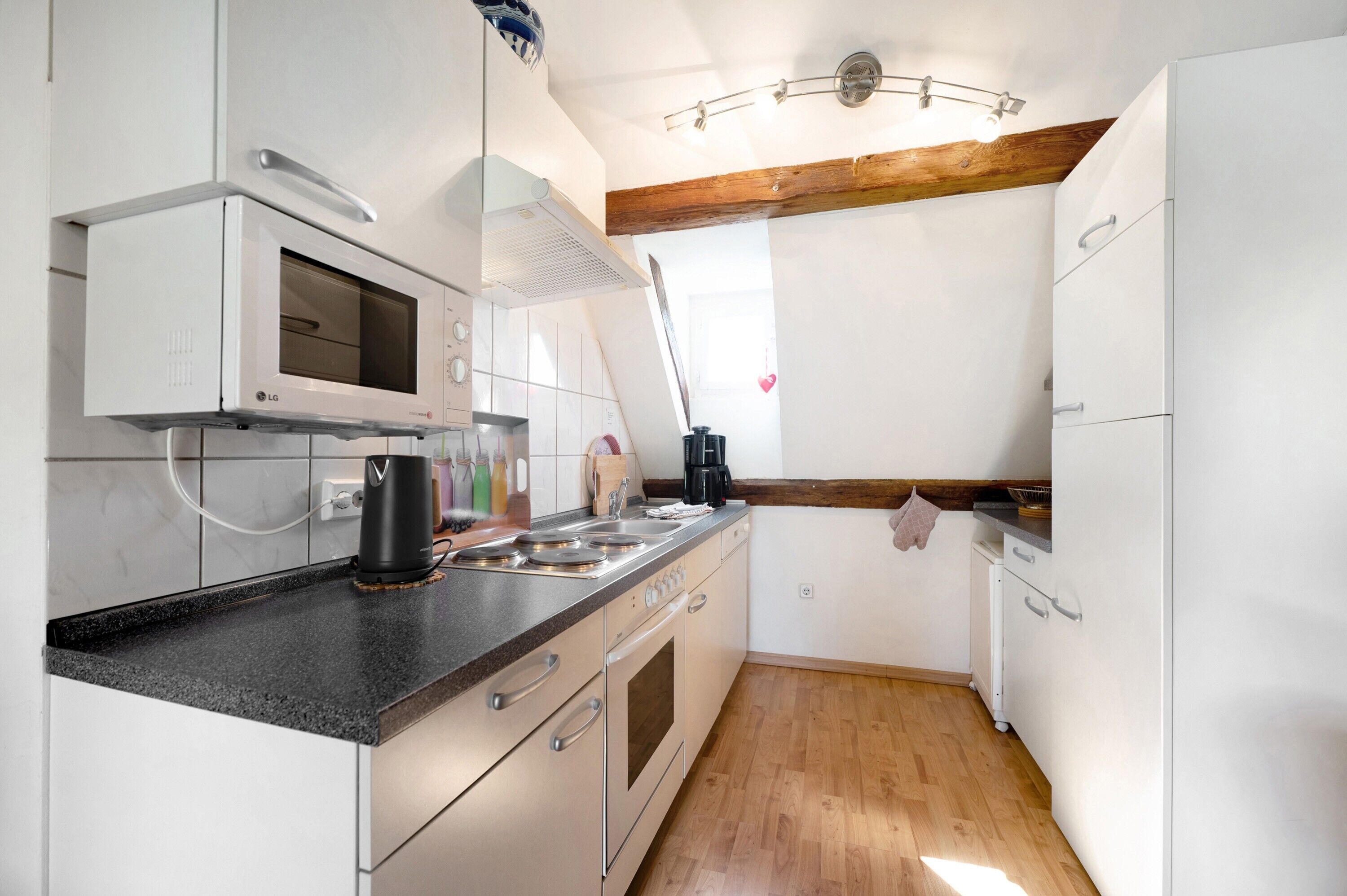 Une cuisine compacte avec des meubles blancs, un four à micro-ondes encastré, une machine à café et un bloc à couteaux.