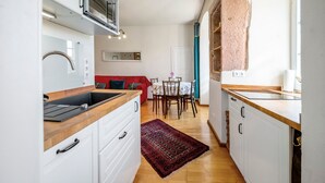 Eine kompakte Küche mit weißen Schränken, einer Mikrowelle und einem Spülbecken. Es gibt eine Essecke mit Tisch und Stühlen sowie ein rotes Sofa.