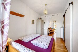 Ein Schlafzimmer mit zwei Betten, einem hölzernen Kopfteil, einer Deckenleuchte, einem Kleiderschrank und einer Tür zu einem weiteren Raum.