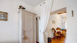 Quarto com um guarda-roupa branco, cortina branca, chão de madeira, uma cadeira e uma pequena mesa.