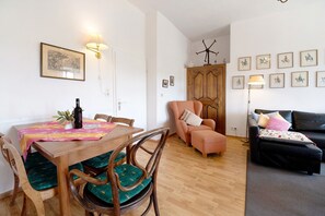 Un coin repas avec une table en bois, des chaises et une lampe. Le salon comprend un canapé et un meuble.