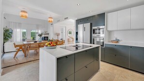 A modern kitchen with a central island, built-in appliances, and a dining area with natural light. - VILLA FALDO VACATION MARBELLA (Nueva Andalucía)