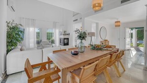 A spacious living area with a wooden dining table, comfortable seating, and a large window offering a view of the outdoors. - VILLA FALDO VACATION MARBELLA (Nueva Andalucía)