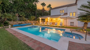 A swimming pool with lounge chairs and a patio area, surrounded by lush greenery and a white building with a tiled roof. - VILLA FALDO VACATION MARBELLA (Nueva Andalucía)