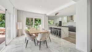 Uma cozinha moderna com uma ilha central, área de refeições com piso de mármore e uma grande porta de vidro deslizante que dá para um pátio externo.