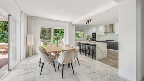 A modern kitchen with a central island, a dining area with a marble floor, and a large sliding glass door leading to an outdoor patio. - VILLA NADAL VACATION MARBELLA (Elviria)