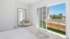 A hotel room with a bed, a chair, a large mirror, and a balcony with a view of greenery. - VILLA NADAL VACATION MARBELLA (Elviria)