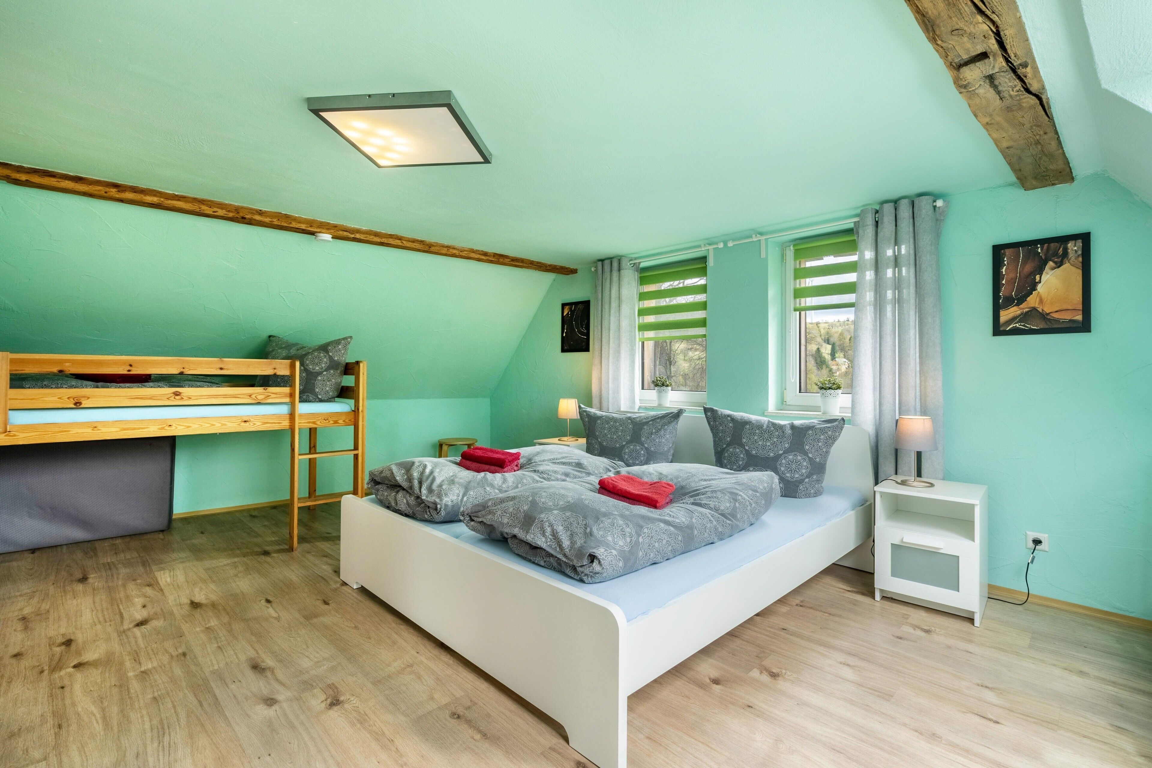 A bedroom with a bunk bed, a single bed, a nightstand, a lamp, and a window with curtains.