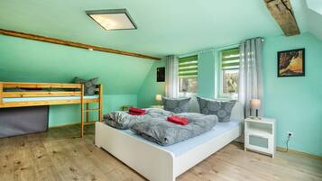 A bedroom with a bunk bed, a single bed, a nightstand, a lamp, and a window with curtains.
