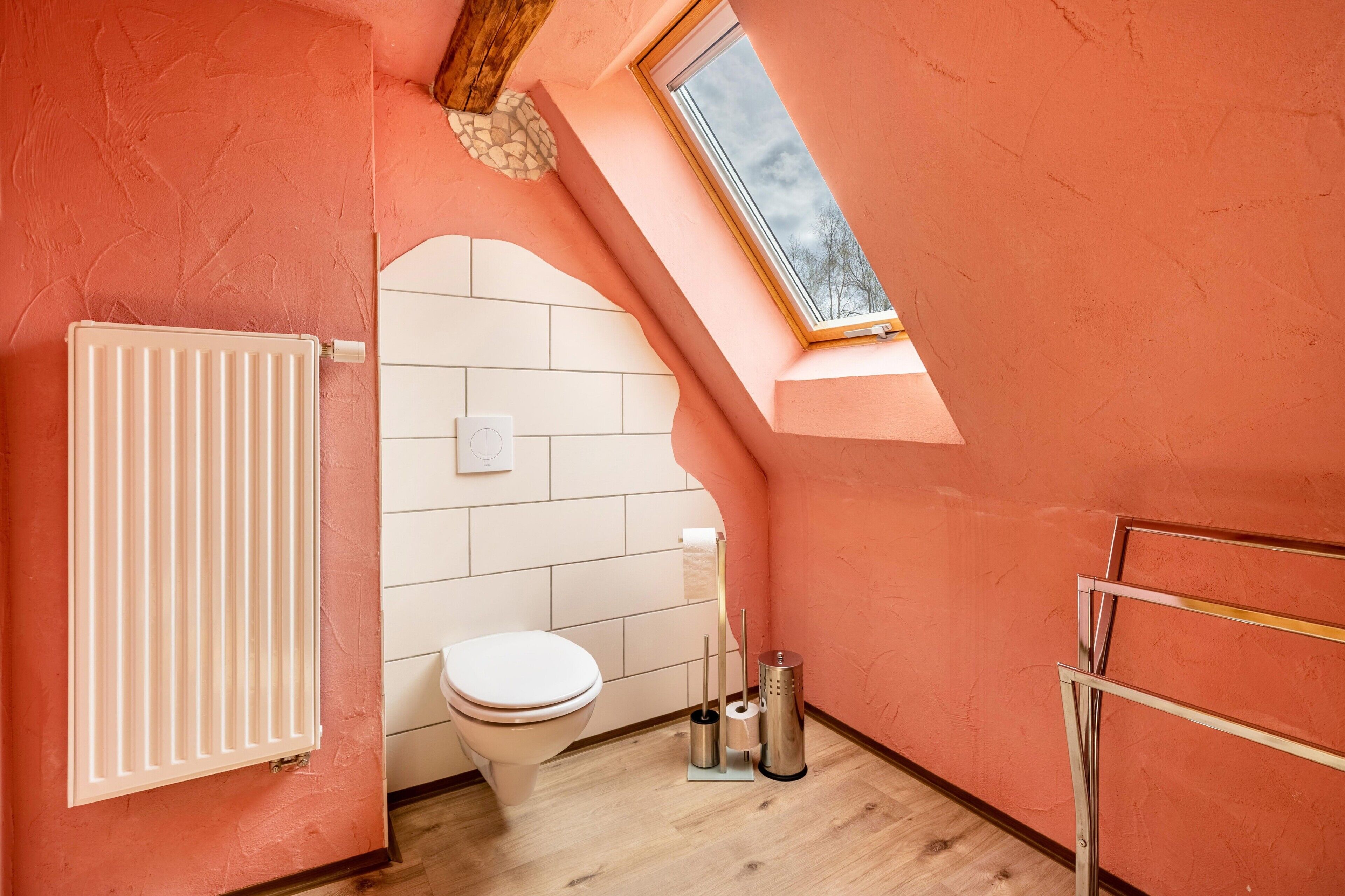 Un baño pequeño y funcional con inodoro blanco, radiador y tragaluz.