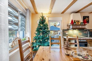 Un coin repas avec une table en bois, des chaises, un sapin de Noël et une cuisine en arrière-plan.