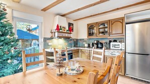 A kitchen with wooden cabinets, a stainless steel refrigerator, and a dining table with chairs. - Apartment 'Ferienhaus Fichtelberg Apartement A' with Mountain View, Private Terrace and Wi-Fi (Oberwiesenthal)