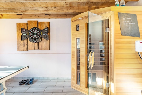 A wooden interior with a ping pong table, a sauna, and a dartboard on the wall.