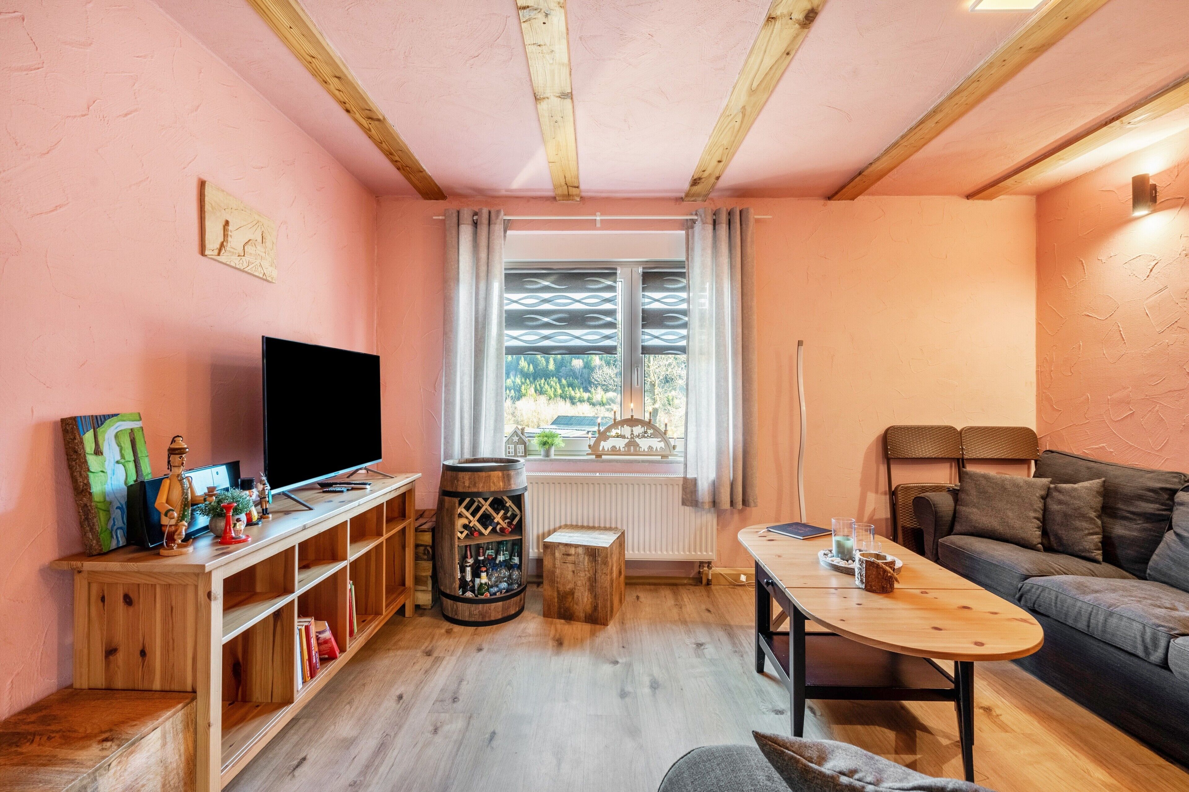Un salón acogedor con techo de madera, televisor, mesa de centro de madera, sofá y una ventana con cortinas.