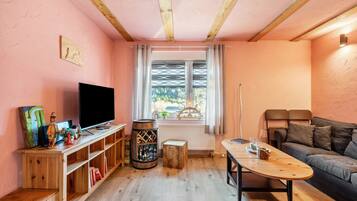 Un salón acogedor con techo de madera, televisor, mesa de centro de madera, sofá y una ventana con cortinas.