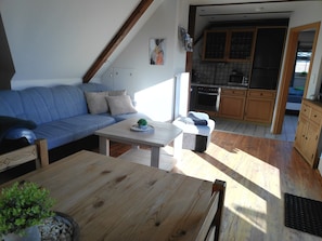 Un espacio de sala acogedor con un sofá, una mesa de madera y una cocina al fondo.