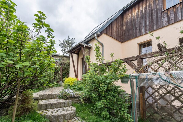 Una casa tradicional con una escalera de piedra, vigas de madera y un jardín con diversas plantas.
