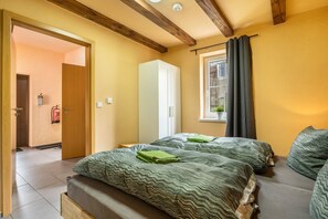 Une chambre avec deux lits, une armoire, une fenêtre avec des rideaux et une porte donnant sur une autre pièce.