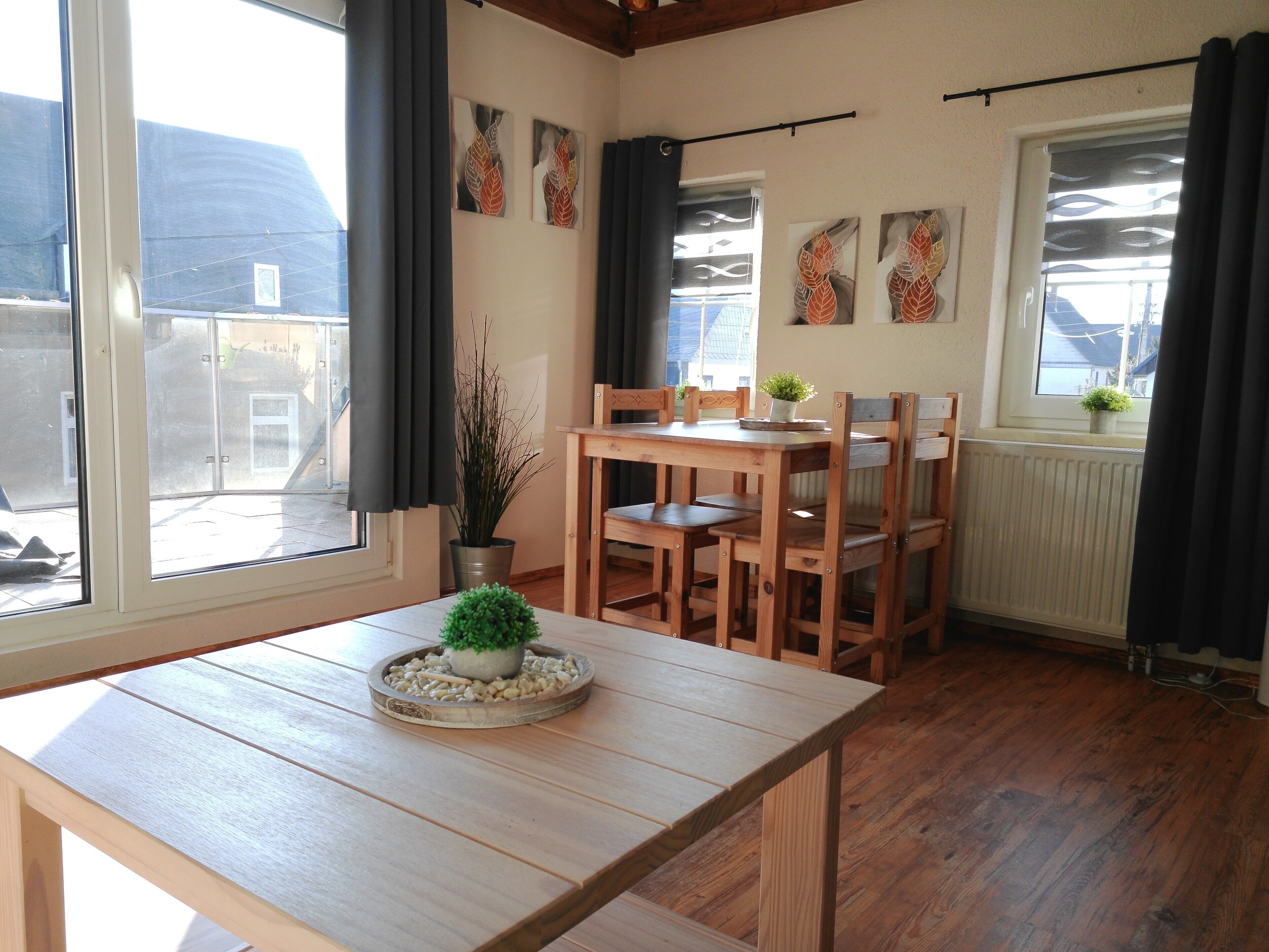 A room with a wooden table, chairs, a potted plant, and artwork on the walls.