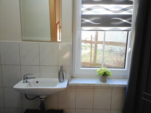 A bathroom with a white sink, a mirror, and a window with a view of the outside.