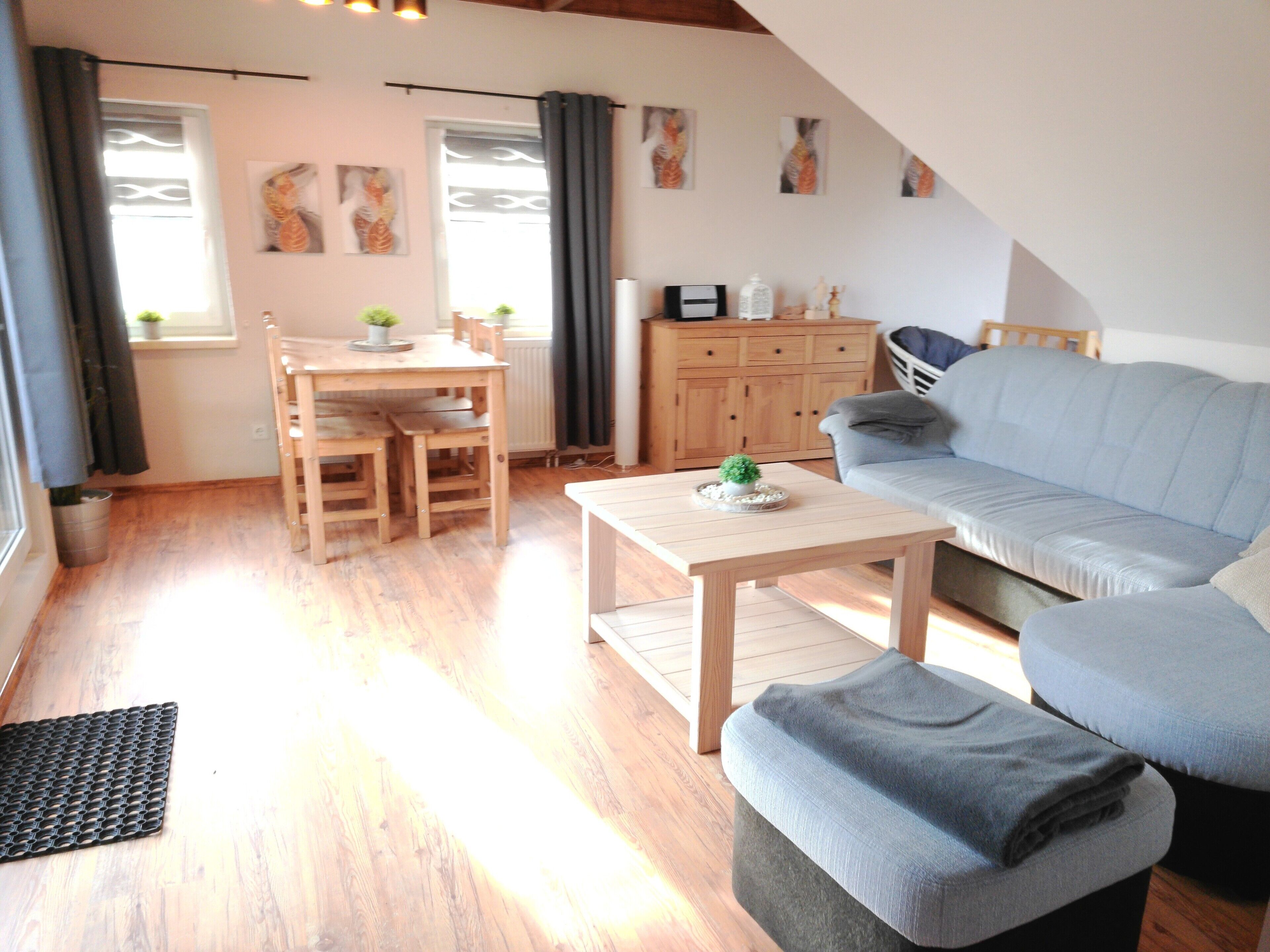 Ein Wohnzimmer mit Holzboden, einer Couch, einem Couchtisch, einem Esstisch mit Stühlen und einem Schrank.